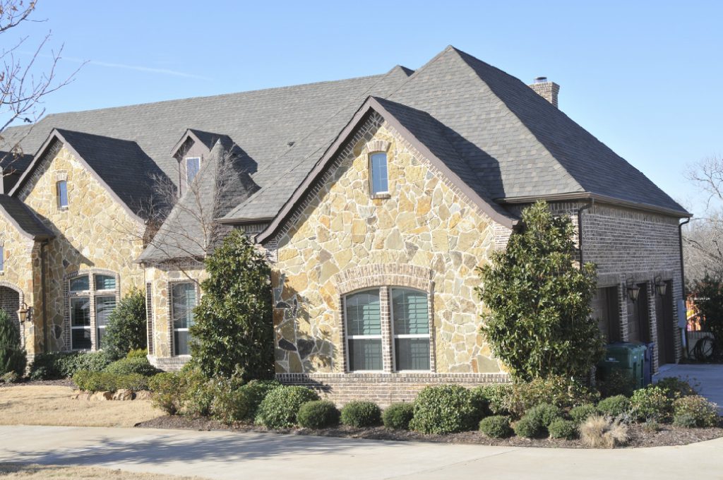 A large stone house with a driveway and bushes.