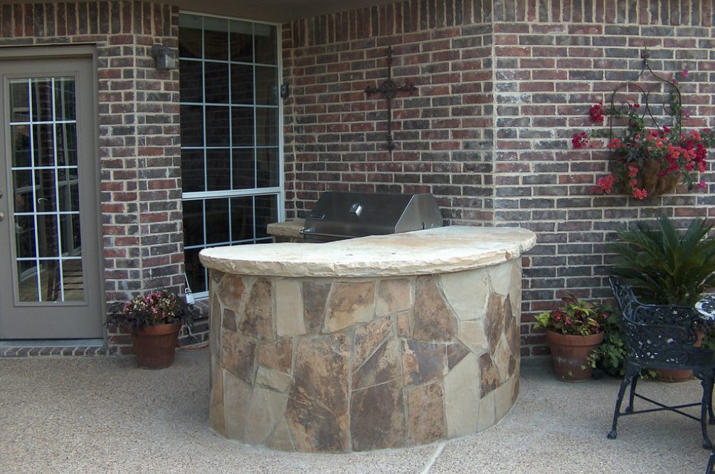 A stone patio with grill and table in the middle.