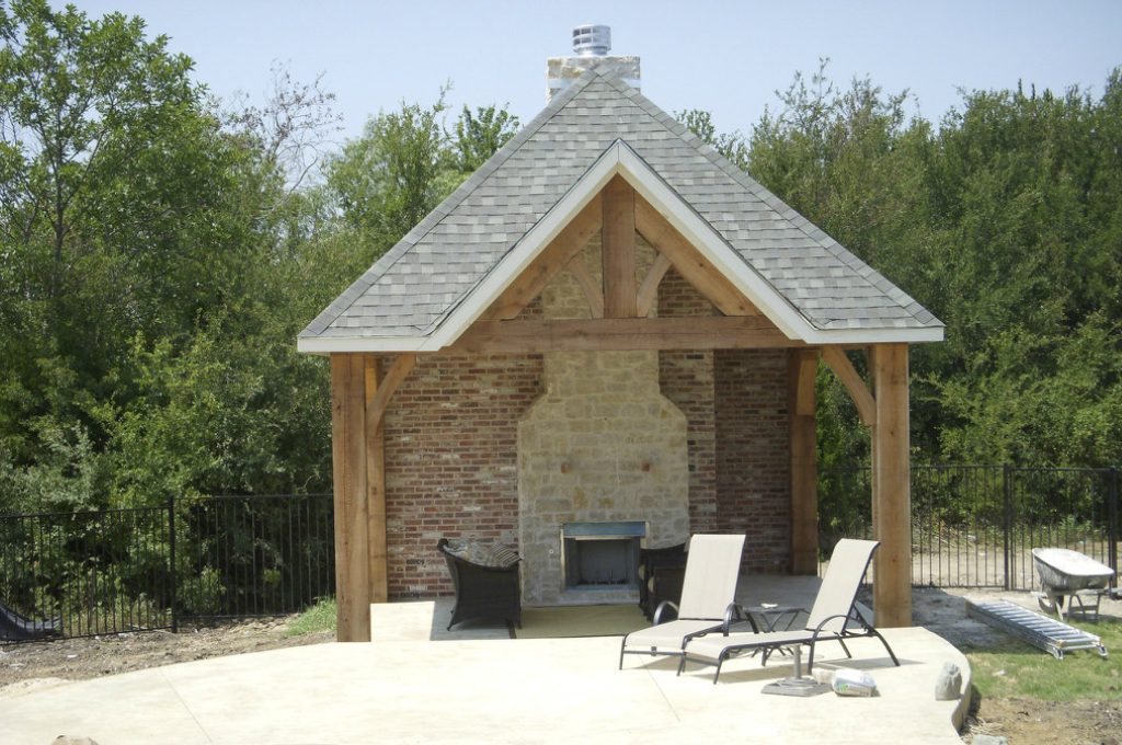 A patio with two lawn chairs and a fireplace.