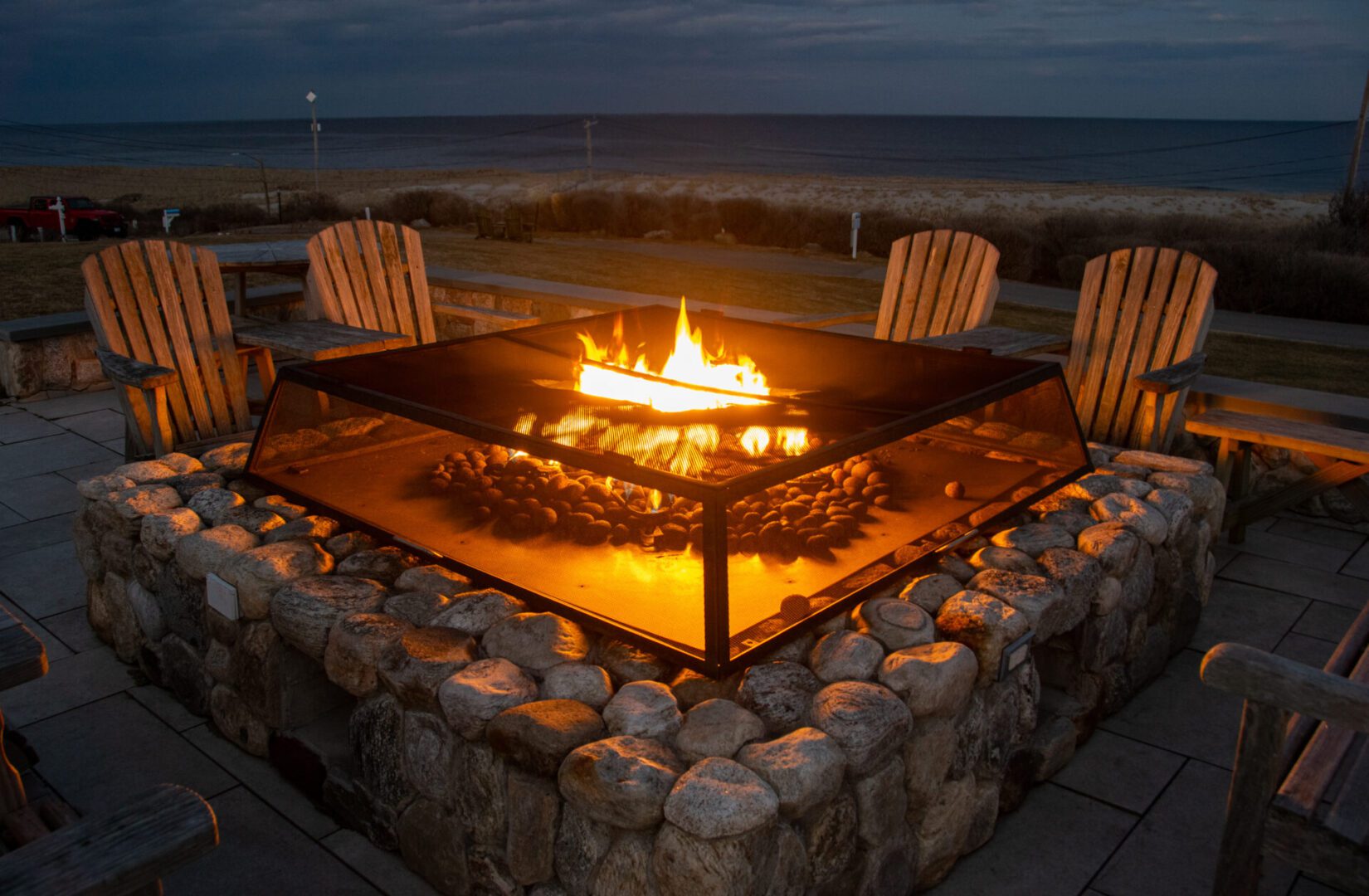 Beachside fire pit with wooden chairs.