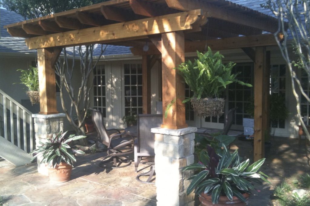 A patio with a wooden pergola and plants.