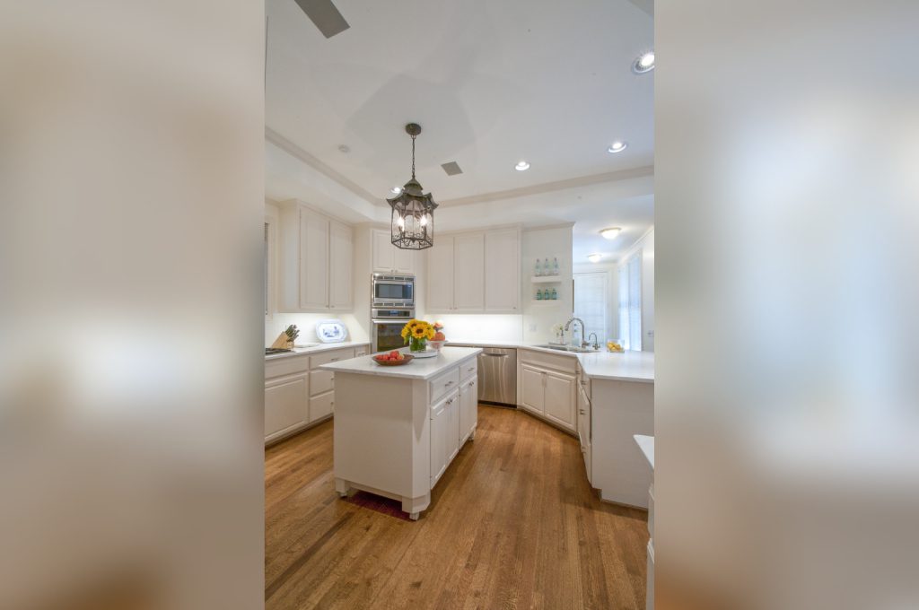 A kitchen with white cabinets and wood floors.