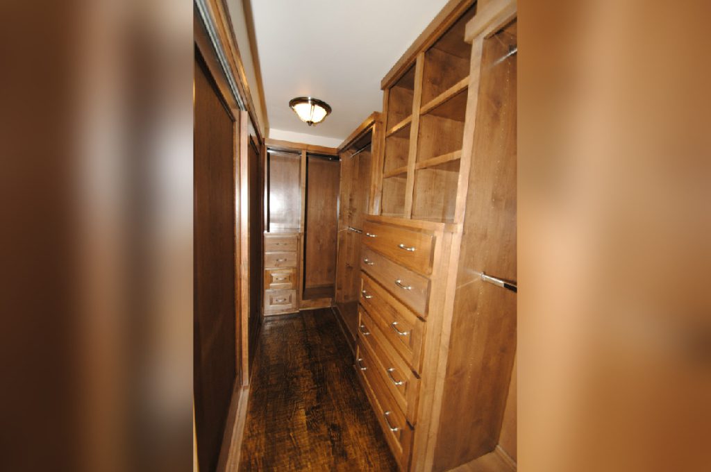 A long walk in closet with wooden floors and drawers.