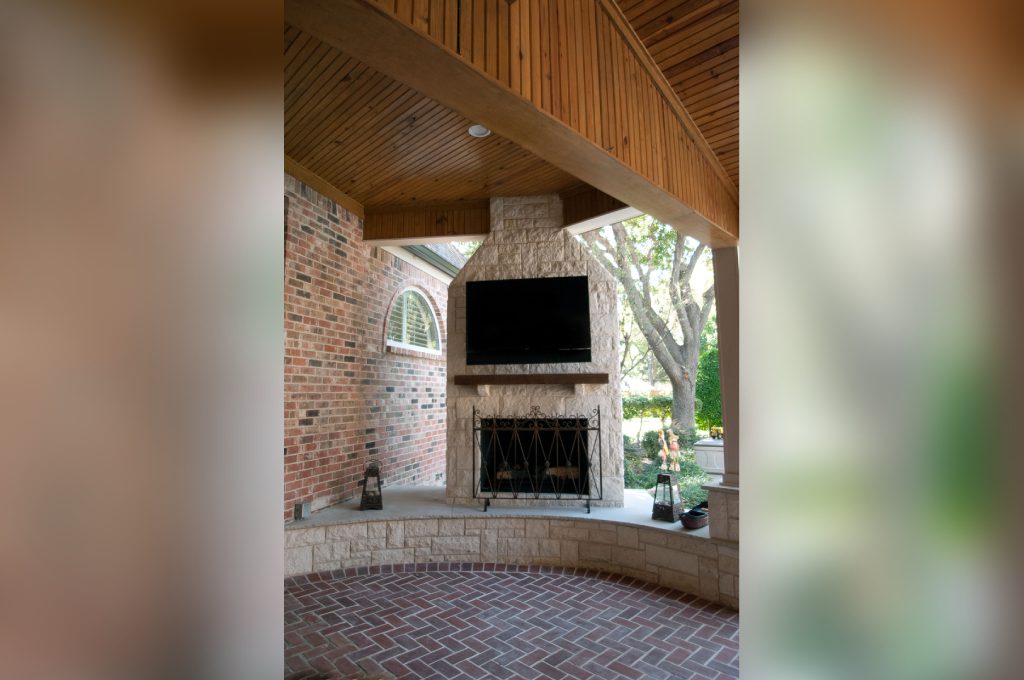 A brick patio with a fireplace and television.